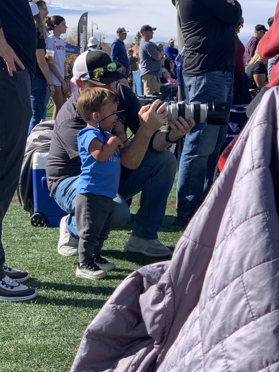 Stan Arnett takes pictures at a lacrosse tournament and has a budding photographer look on.